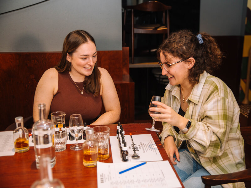 Two women tasting amber-coloured alcohol